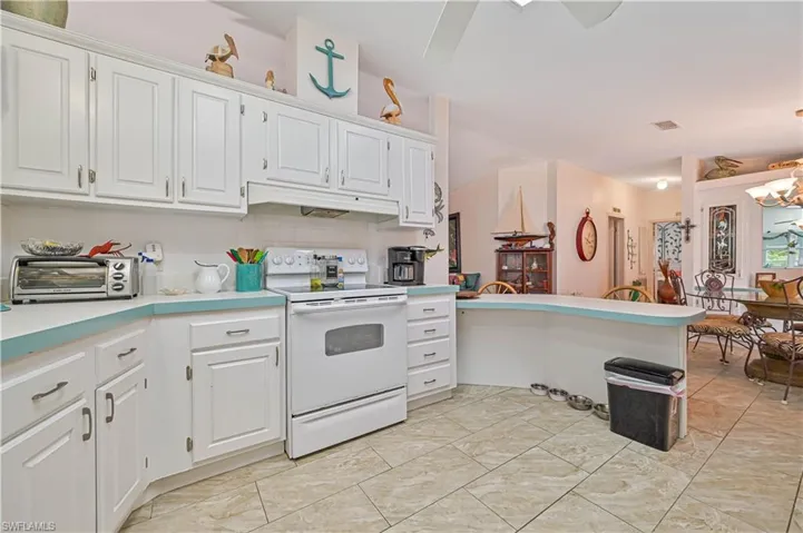 Kitchen with light countertops, under cabinet range hood, a chandelier, a toaster, and white range with electric cooktop