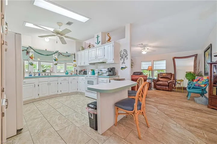 Kitchen featuring light countertops, visible vents, white appliances, a ceiling fan, and a breakfast bar area
