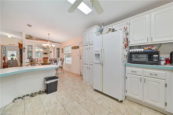 Kitchen with black microwave, white refrigerator with ice dispenser, white cabinetry, visible vents, and decorative light fixtures