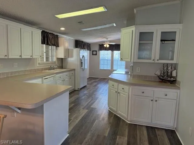 Kitchen with kitchen peninsula, dark wood-type flooring, ceiling fan, and fridge
