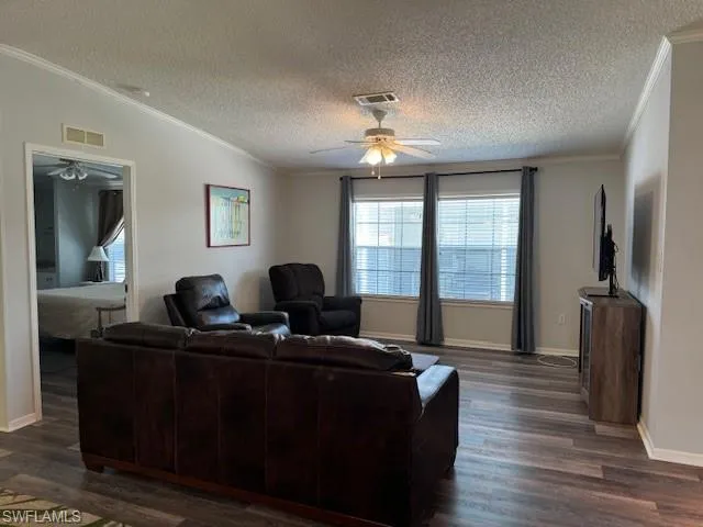 Living room with a textured ceiling, ornamental molding, ceiling fan, and dark hardwood / wood-style flooring