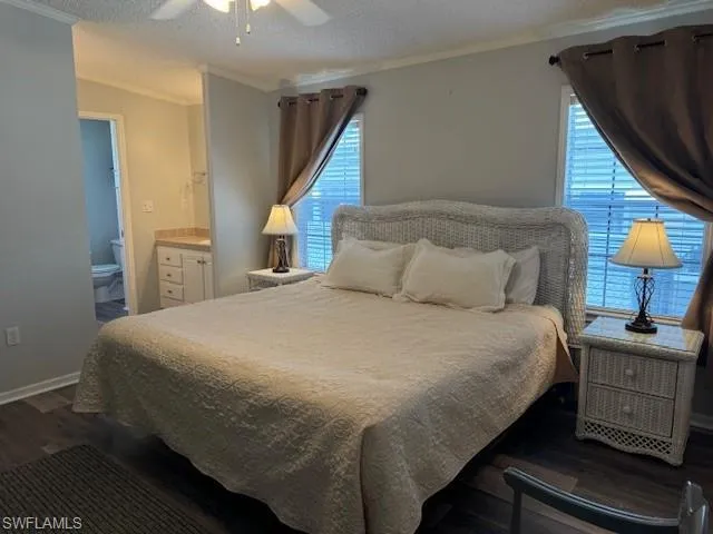 Bedroom featuring dark wood-type flooring, connected bathroom, ceiling fan, and multiple windows