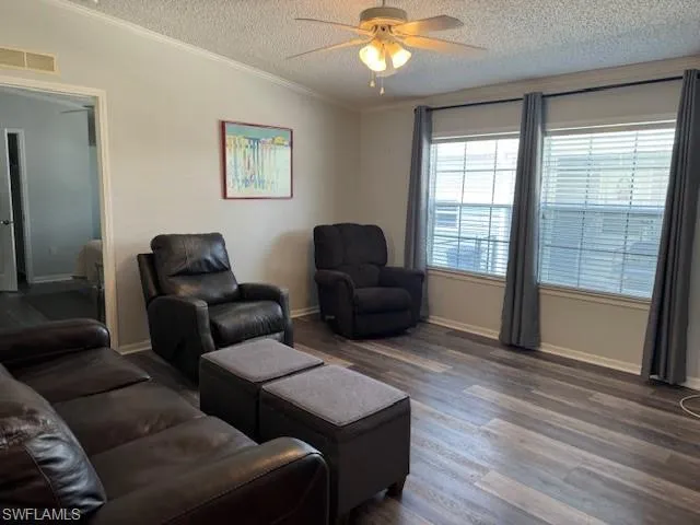 Living room featuring ceiling fan, ornamental molding, a textured ceiling, and dark wood-type flooring