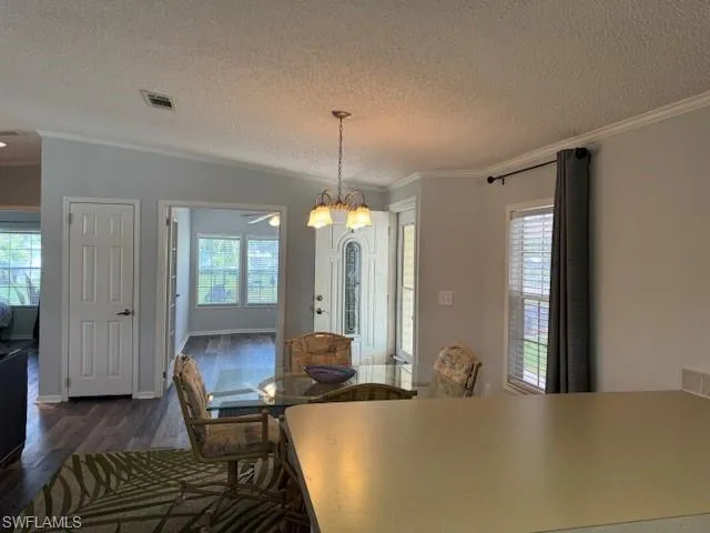 Dining area with a notable chandelier, a textured ceiling, dark hardwood / wood-style floors, and crown molding