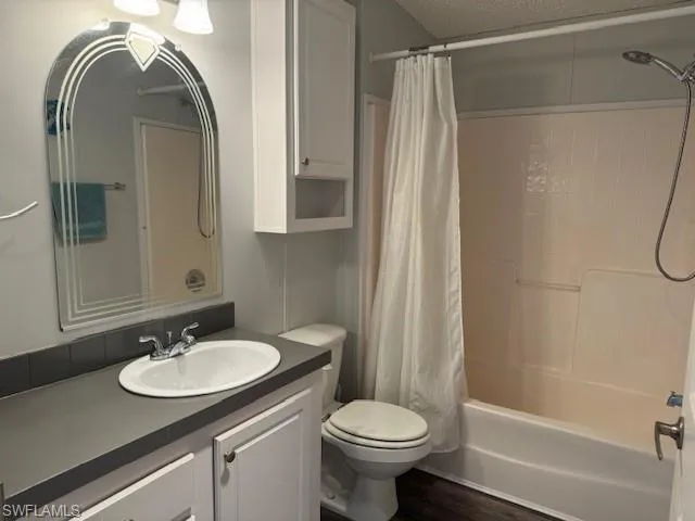 Full bathroom featuring toilet, hardwood / wood-style floors, shower / bath combo with shower curtain, vanity, and a textured ceiling