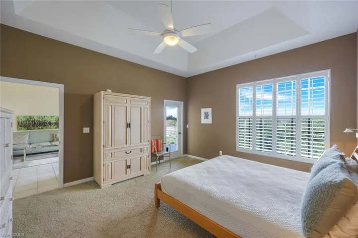 Carpeted Master bedroom featuring ceiling fan, a raised ceiling, and multiple windows