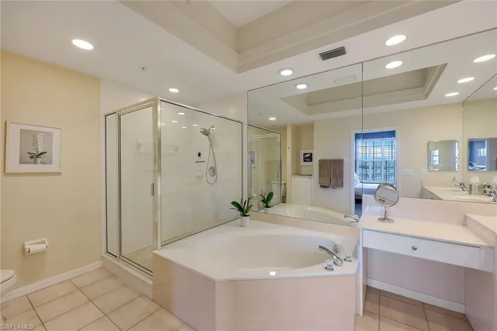 Full bathroom featuring vanity, a raised tray ceiling, tile flooring, toilet, and shower with separate bathtub