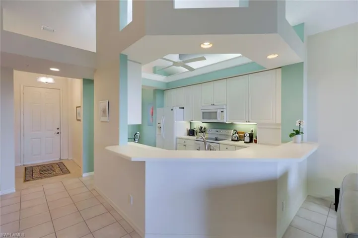 Kitchen featuring kitchen peninsula, light tile patterned floors, white appliances, and white cabinetry