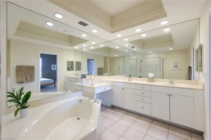 Bathroom featuring a tray ceiling, tile patterned floors, vanity, and separate shower and bath