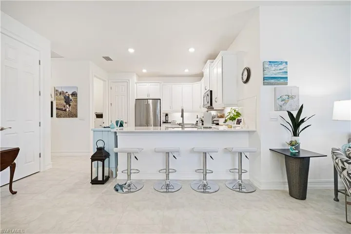 Kitchen with appliances with stainless steel finishes, a peninsula, a kitchen bar, white cabinets, and light countertops
