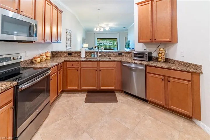 Kitchen with stainless steel appliances, sink, crown molding, vaulted ceiling, and an inviting chandelier