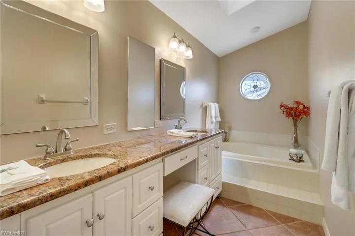 Bathroom featuring vanity, vaulted ceiling, tile patterned floors, and a relaxing tiled tub