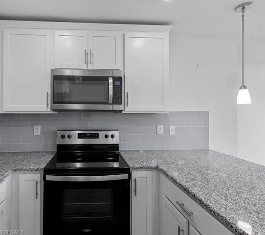 Kitchen with stainless steel appliances, white cabinets, decorative light fixtures, light stone countertops, and tasteful backsplash