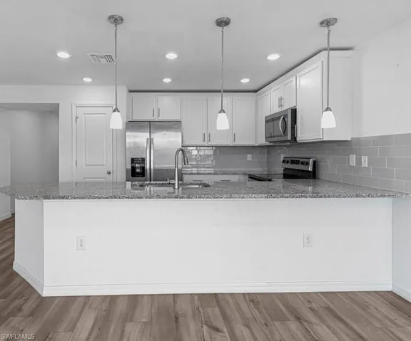 Kitchen with a peninsula, light stone counters, stainless steel appliances, white cabinetry, and light wood-style flooring