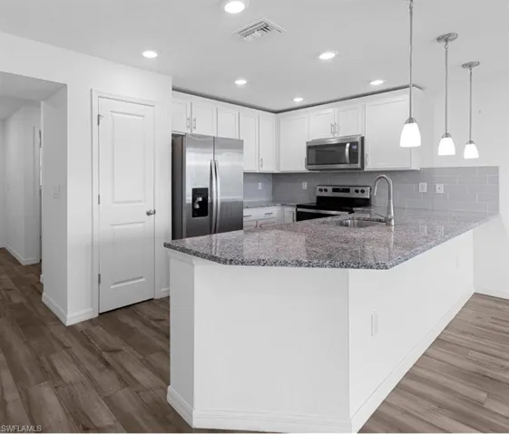 Kitchen with dark stone counters, stainless steel appliances, a peninsula, white cabinetry, and light wood-style flooring