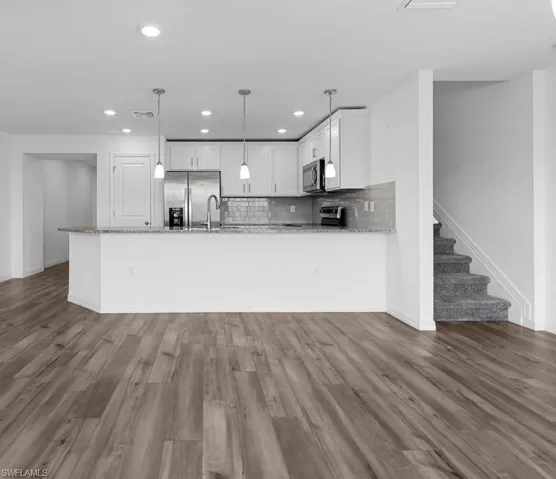 Kitchen featuring stainless steel appliances, light stone counters, backsplash, a peninsula, and dark wood-style floors