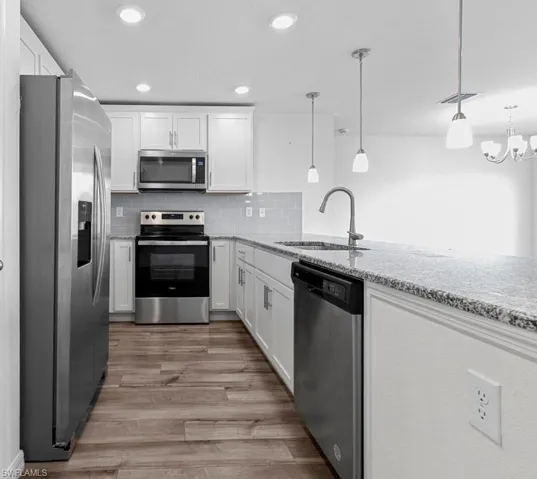 Kitchen with stainless steel appliances, white cabinetry, light stone counters, a peninsula, and light wood-type flooring