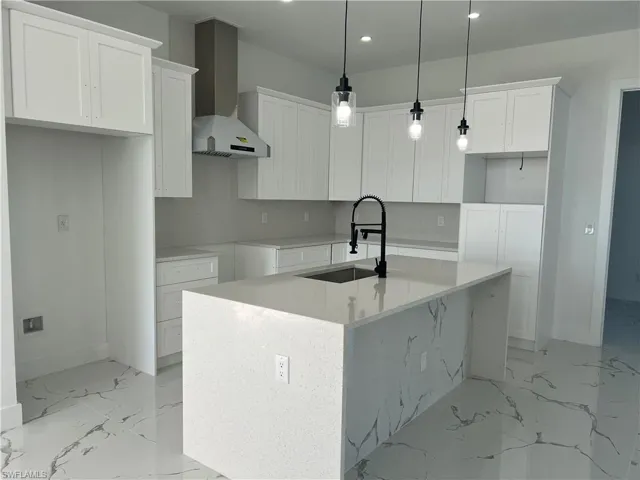 Kitchen with white cabinets, sink, a kitchen island with sink, and wall chimney range hood