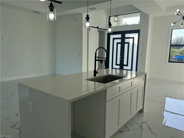 Kitchen featuring a center island with sink, hanging light fixtures, a barn door, light stone countertops, and white cabinetry