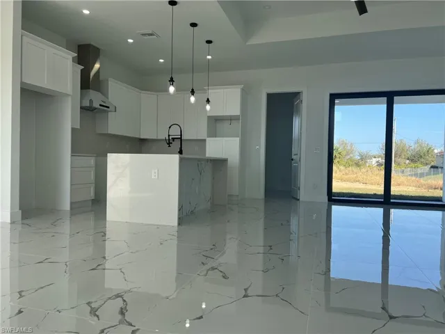 Kitchen with white cabinets, wall chimney exhaust hood, pendant lighting, and a center island
