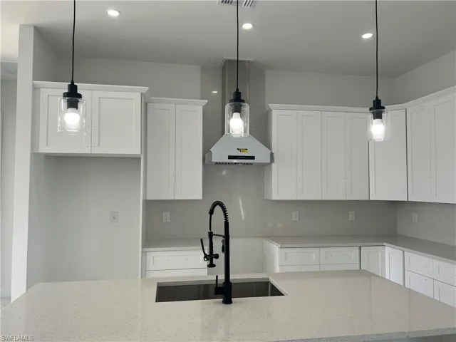 Kitchen with light stone countertops, decorative light fixtures, and white cabinetry
