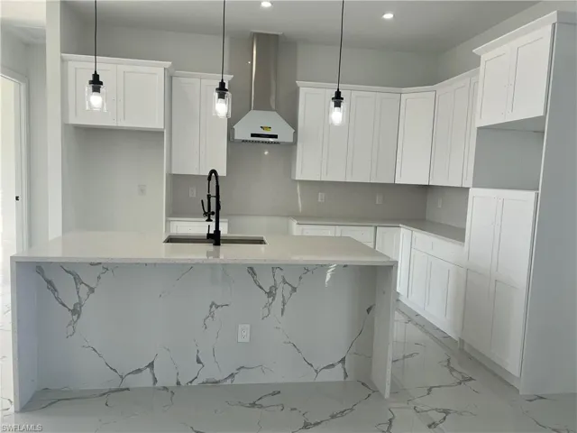 Kitchen featuring pendant lighting, wall chimney exhaust hood, and a kitchen island with sink