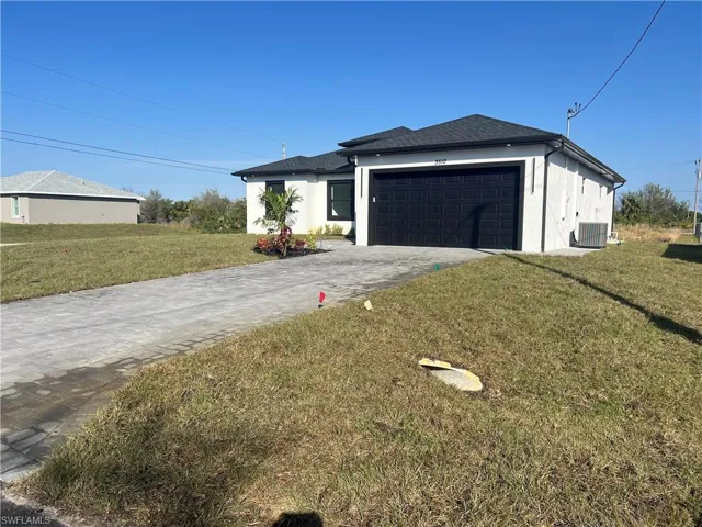 View of front of home with cooling unit, a garage, and a front lawn