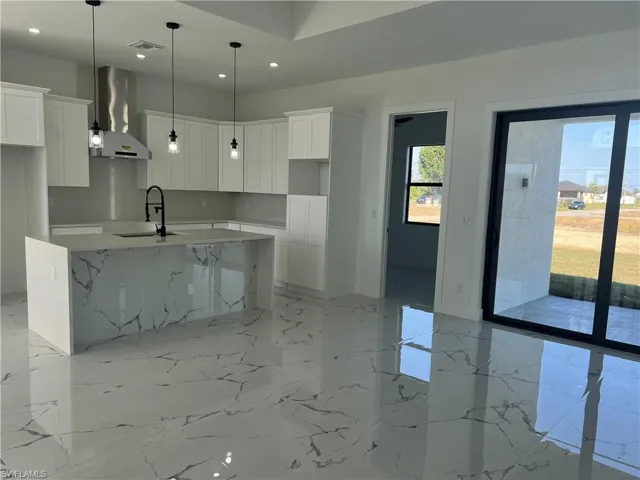 Kitchen with white cabinets, a center island with sink, wall chimney range hood, and sink