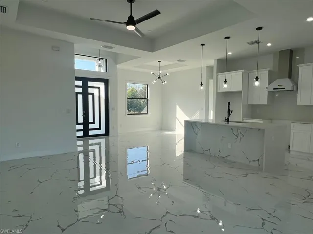 Kitchen with white cabinets, wall chimney exhaust hood, sink, and decorative light fixtures