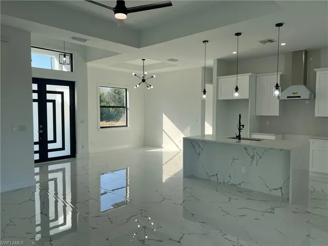 Kitchen with a kitchen island with sink, white cabinetry, wall chimney exhaust hood, and light stone countertops