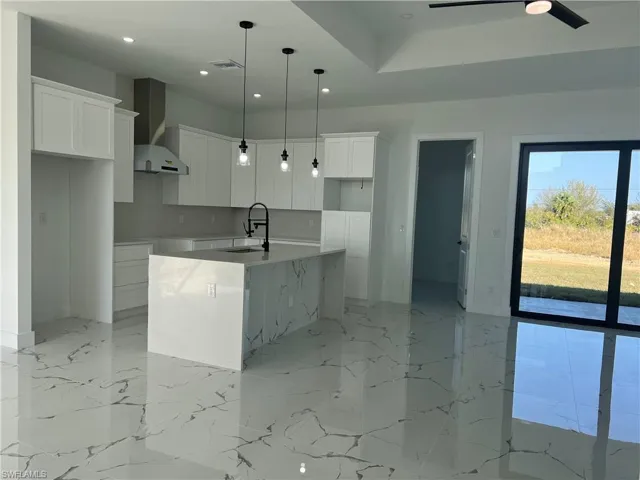 Kitchen with a kitchen island with sink, white cabinets, sink, hanging light fixtures, and wall chimney exhaust hood