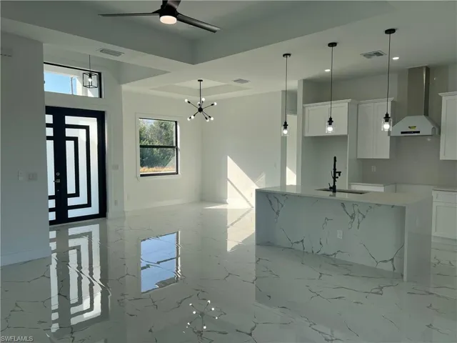 Kitchen featuring light stone countertops, sink, wall chimney range hood, a kitchen island with sink, and white cabinets