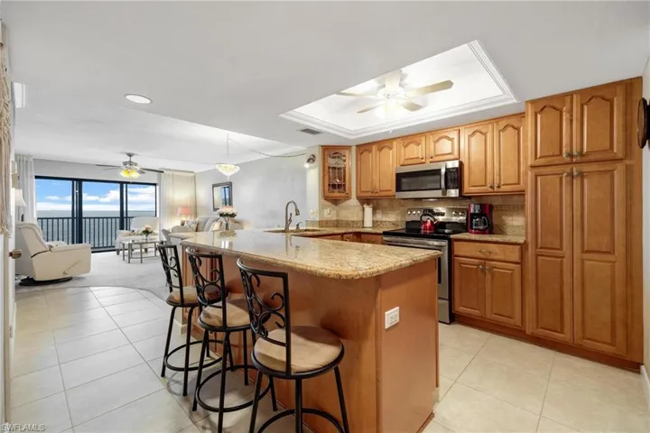 Kitchen featuring stainless steel appliances, ceiling fan, a tray ceiling, and tasteful backsplash