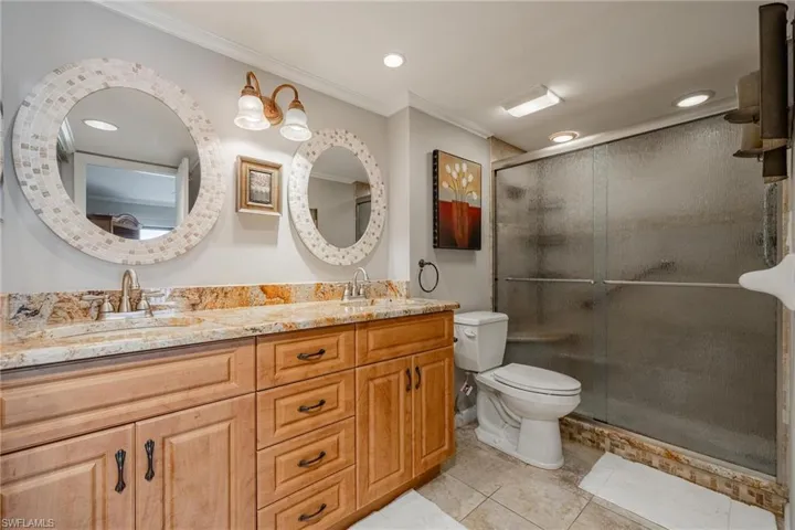 Bathroom with double sink, tile floors, a shower with door, large vanity, and toilet