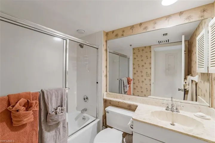 Full bath with wallpapered walls, combined bath / shower with glass door, and vanity