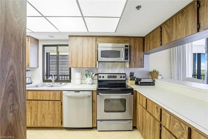 Kitchen with appliances with stainless steel finishes, light countertops, backsplash, light tile patterned floors, and brown cabinets