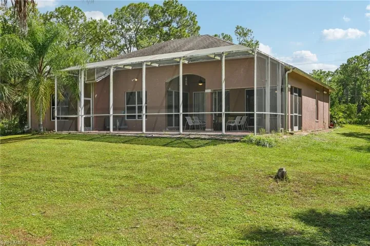 Rear view of house with a yard, stucco siding, a sunroom, and glass enclosure