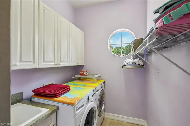 Laundry room featuring washing machine and dryer, light tile patterned floors, and cabinet space