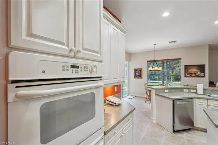 Kitchen with white oven, white cabinets, recessed lighting, light tile patterned floors, and pendant lighting