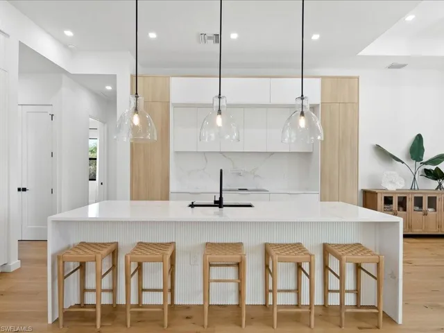 Kitchen with light stone counters, light wood-style floors, decorative light fixtures, and recessed lighting