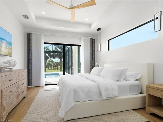 Bedroom featuring light wood finished floors, access to outside, multiple windows, and a raised ceiling