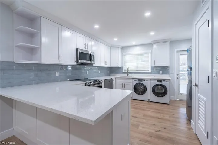Contemporary kitchen featuring white shaker cabinetry, light-toned wood-finish flooring, and a comprehensive appliance suite