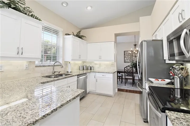 Kitchen featuring white cabinets, stainless steel appliances, light stone counters, lofted ceiling, and decorative backsplash