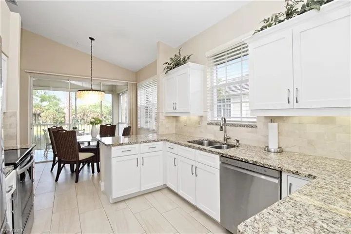 Kitchen featuring stainless steel appliances, white cabinets, lofted ceiling, light stone countertops, and backsplash