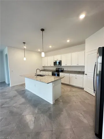 Kitchen with decorative light fixtures, appliances with stainless steel finishes, a center island with sink, dark stone counters, and white cabinetry