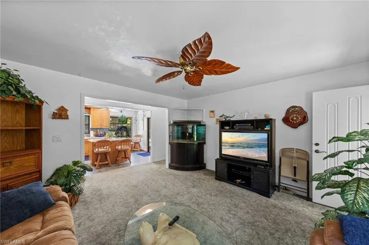 Expansive living area featuring a ceiling fan with leaf-shaped blades, light-toned carpeting, and a white entry door