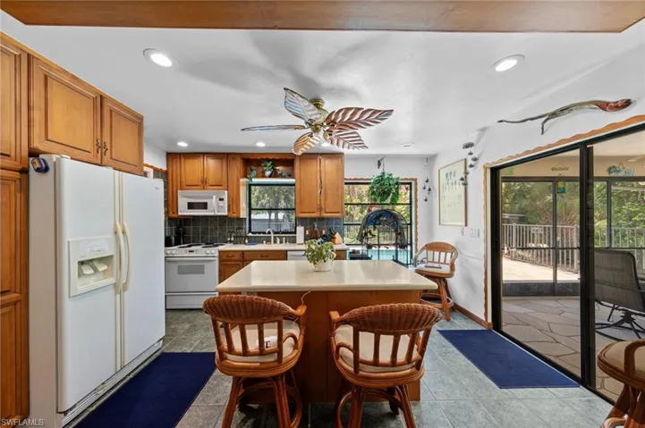 Kitchen featuring wood cabinetry, white appliances, a center island with countertop seating, and recessed lighting