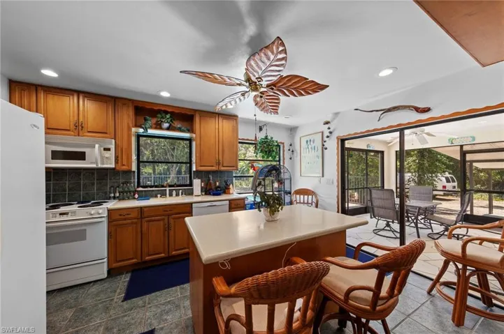 Kitchen with wood cabinetry, white appliances, and a central island with a light-colored countertop