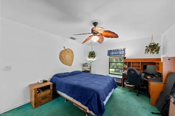 Bedroom featuring a ceiling fan with integrated lighting, a built-in desk with shelving, and a window offering exterior views