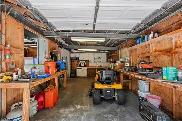 Versatile garage space featuring exposed wood paneling, overhead fluorescent lighting, a roll-up garage door, built-in shelving, and a dedicated workspace with built-in cabinetry and a utility sink